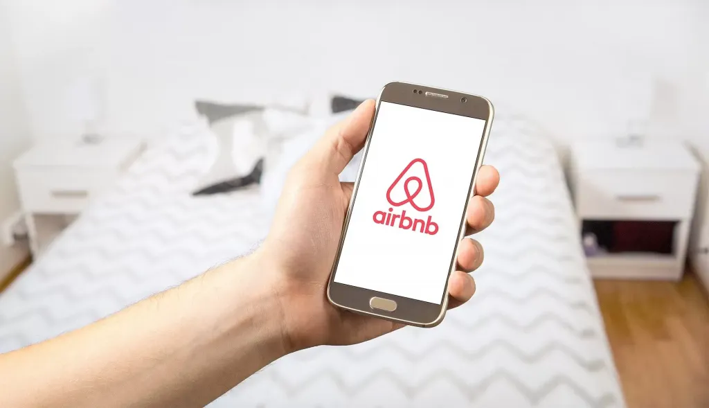 Airbnb logo in the screen of a phone in front of a bed