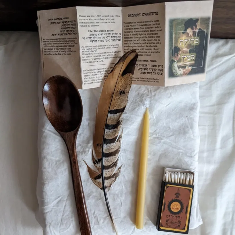 Spoon feather candle matches and an hebrew booklet over a white cloth